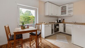 Cucina con mobili bianchi, un tavolo di legno e una finestra vista verde.