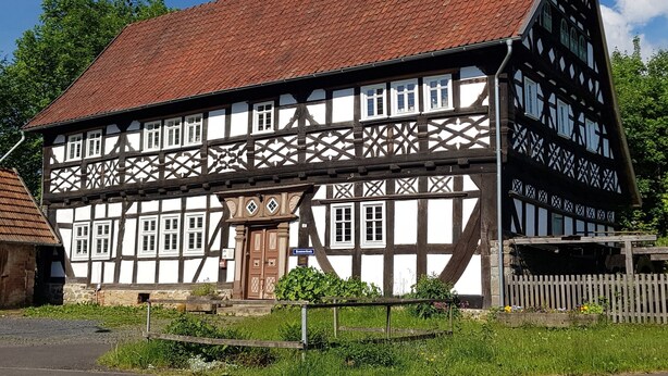 Ein traditionelles Fachwerkhäuschen mit steilem Dach, zahlreichen Fenstern und einem gut sichtbaren Eingang.