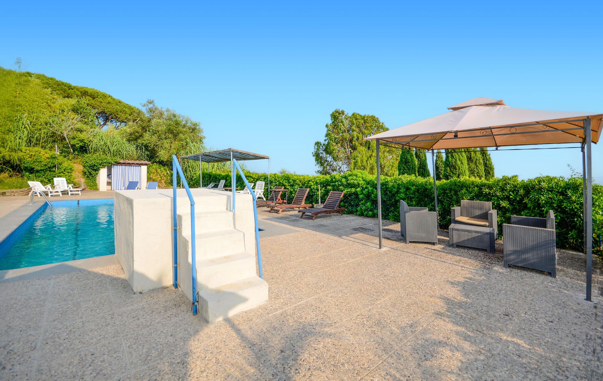 A pool area with a diving board, lounge chairs, and a covered seating area.