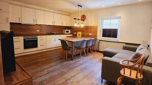 A modern kitchen with wooden cabinets, a dining table with chairs, a sofa, and a rocking chair. - Apartment 'Huhn' with Shared Terrace, Shared Garden and Wi-Fi (Schmallenberg)