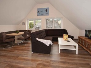 A loft-style living space with a dark brown sectional sofa, a white coffee table, and a dining area with a wooden table and chairs. - Apartment 'Schwalbe' with Mountain View, Shared Terrace and Wi-Fi (Schmallenberg)