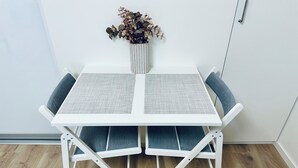 A white foldable table with grey cushions, a vase with dried flowers, and a wooden floor. - Katariina Apartments (Kotka)