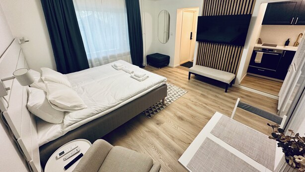 A hotel room with a bed, bedside table, lamp, and a small seating area. - Katariina Apartments (Kotka)