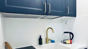 A kitchen with a white countertop, a Bosch induction cooktop, a gold faucet, and dark blue cabinets. - Katariina Apartments (Kotka)