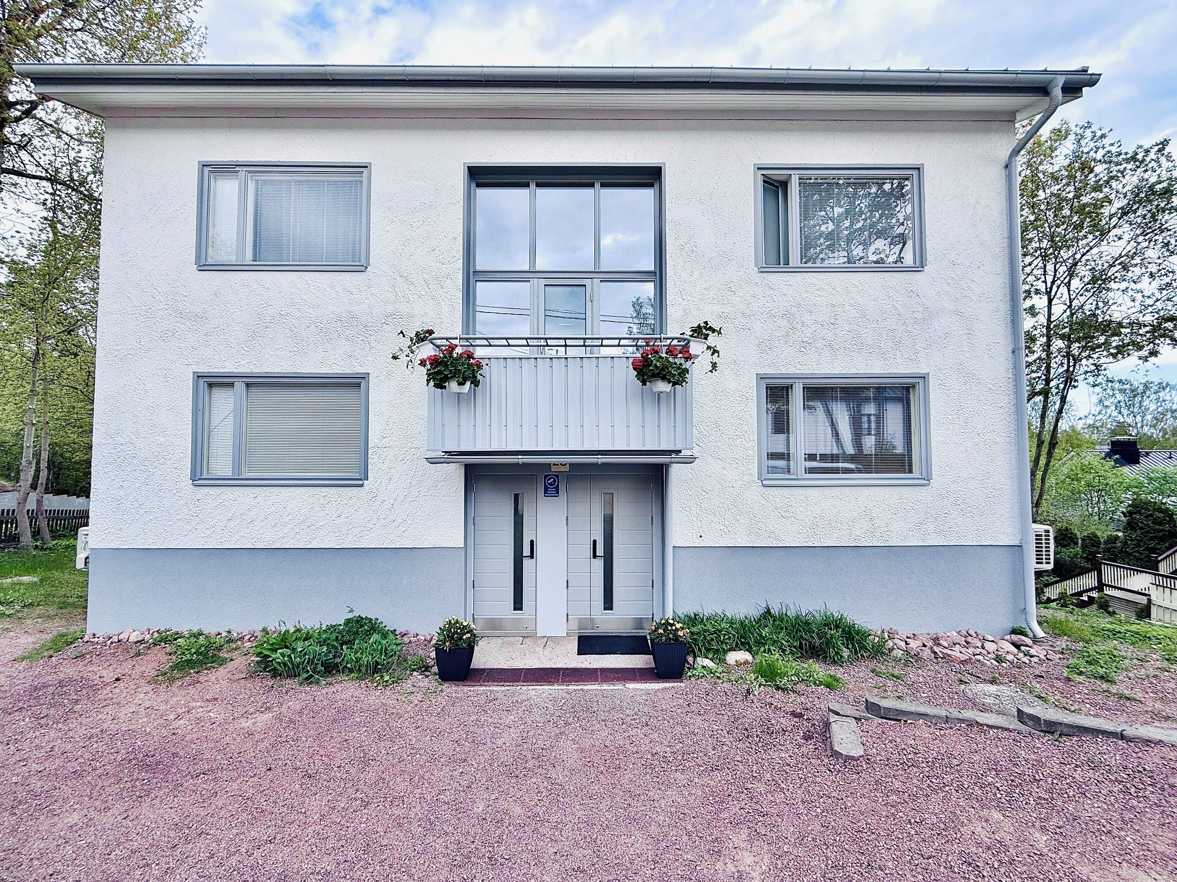 A two-story building with a white exterior, a balcony with flower boxes, and a front door with a small step leading up to it.