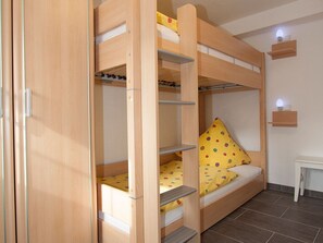 Een stapelbed met een bureau en een plankensysteem, een klein nachtkastje en een wandlamp.