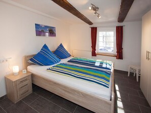 A bedroom with a bed, a nightstand, a bedside lamp, a window with curtains, and a painting on the wall. - Apartment 'Katze' with Shared Terrace, Shared Garden and Wi-Fi (Schmallenberg)