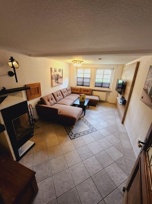 A living room with a sectional sofa, a television, a fireplace, and a window with blinds. - Apartment 'Katze' with Shared Terrace, Shared Garden and Wi-Fi (Schmallenberg)