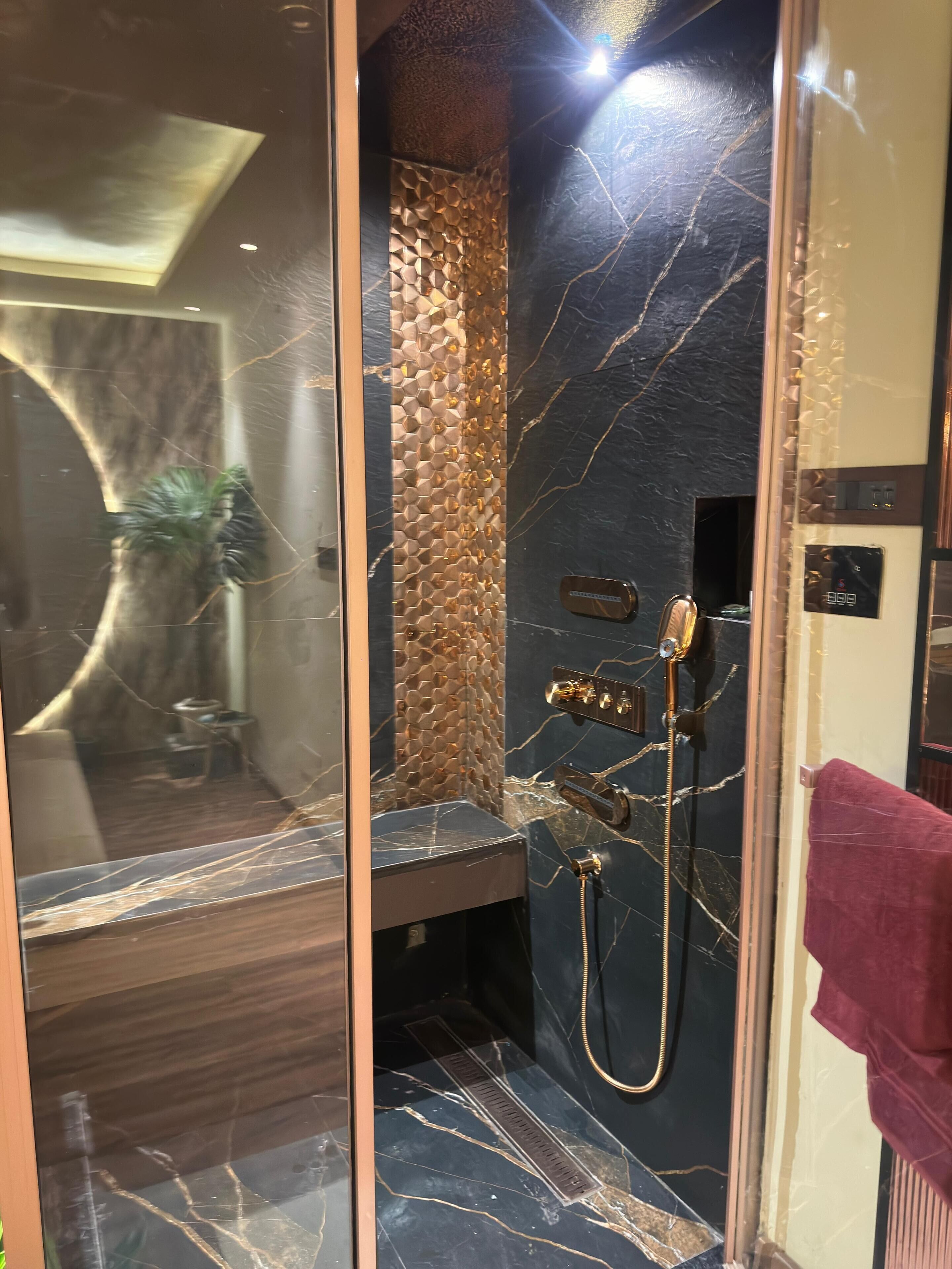 A modern bathroom with a marble vanity, a shower with a gold shower head, and a textured wall.