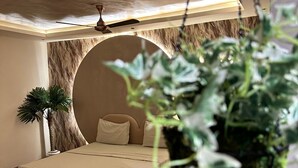 A modern bedroom with a hanging bed, a small seating area, and a large potted plant. - Dream Desire (New Delhi)