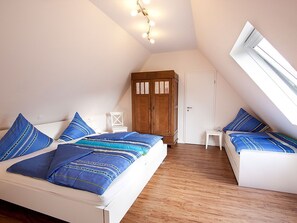Ein Schlafzimmer mit schrägen Wänden, einem Kleiderschrank, einem kleinen Tisch und zwei Betten mit passender blauer Bettwäsche.