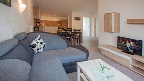 A modern living room with a sectional sofa, a flat-screen TV, a coffee table, and a dining area in the background. - Apartment 'Kuhstall' with Shared Terrace, Shared Garden and Wi-Fi (Schmallenberg)