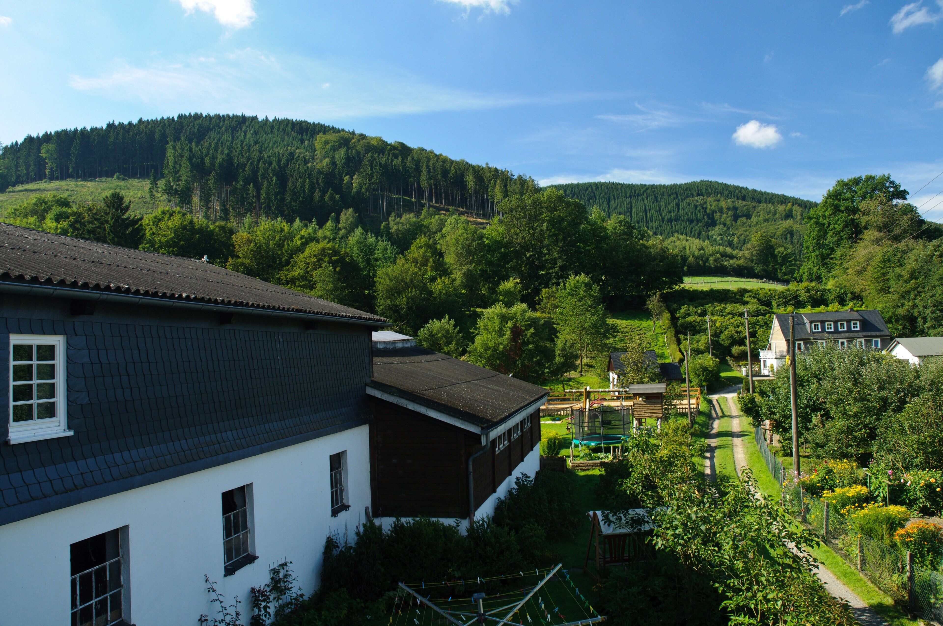 A rural setting with a house, a path, and a forested hill.