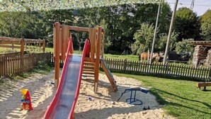 A playground with a slide, sand, and toy vehicles.