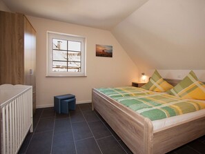 Een slaapkamer met een bed, een raam, een nachtkastje, een kleine tafel en een wieg.