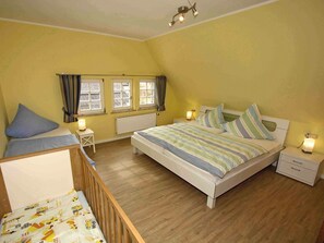 A bedroom with a large bed, bedside tables, a crib, and a window with curtains. - Apartment 'Ziege' with Mountain View, Shared Terrace and Wi-Fi (Schmallenberg)