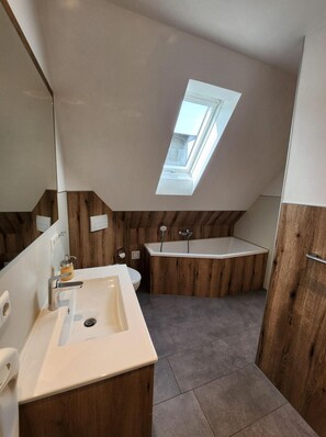A modern bathroom with a skylight, a bathtub, and a vanity with a mirror. - Apartment 'Ziege' with Mountain View, Shared Terrace and Wi-Fi (Schmallenberg)