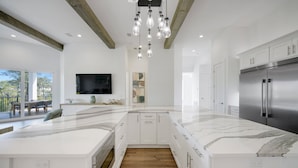 A modern kitchen with white cabinetry, a large island, and a stainless steel refrigerator. - Sleeps 39 | 2 Luxe Homes w/ Free Golf Cart, Private Pool+Spa | 3 Blocks to Beach (Santa Rosa Beach)