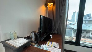 A hotel room with a desk, a television, a cup, and a window with a city view.