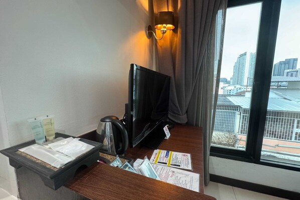 A hotel room with a desk, a television, a cup, and a window with a city view.