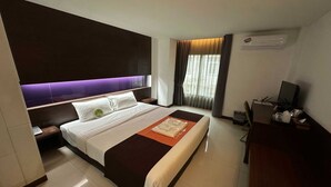 A hotel room with a large bed, a desk with a computer, and a window with curtains.