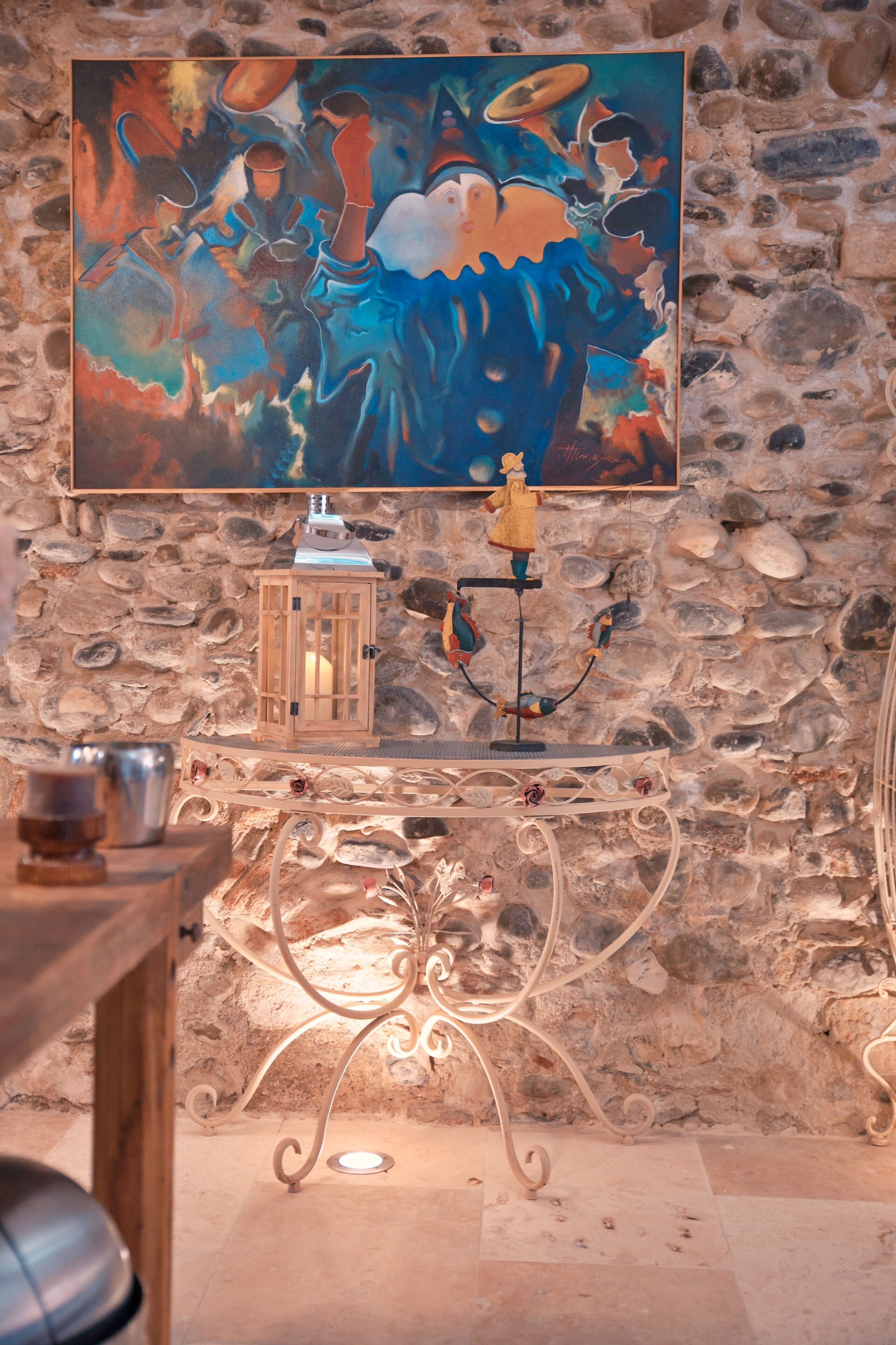 Un mur de pierre orné d’une peinture, une lanterne et une table en métal avec un chandelier.