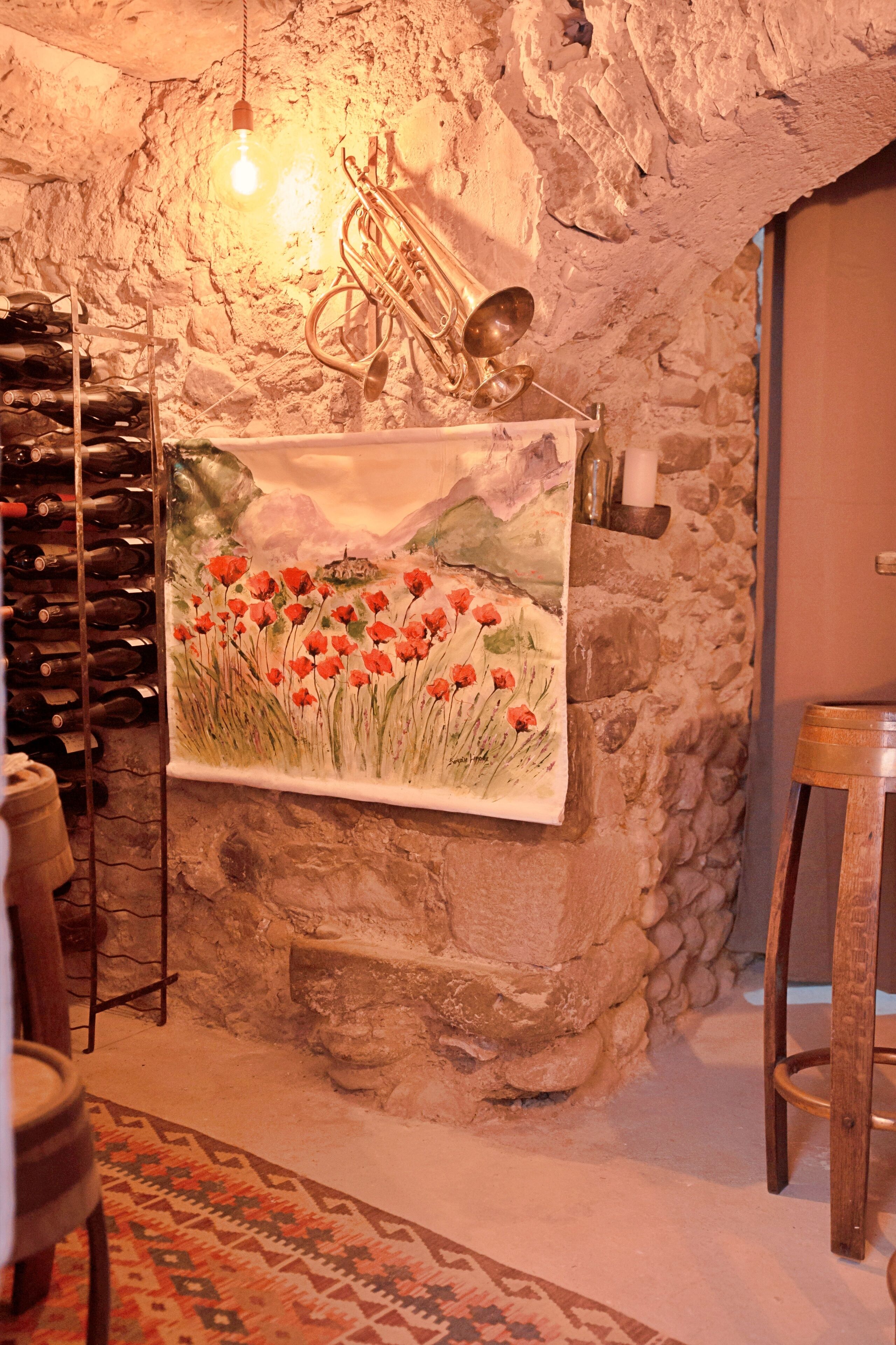 A stone wall with a hanging light bulb, a trumpet, and a wine rack.