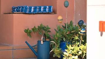 Een balkon met potplanten, een blauwe gieter en een blauwe stoel.