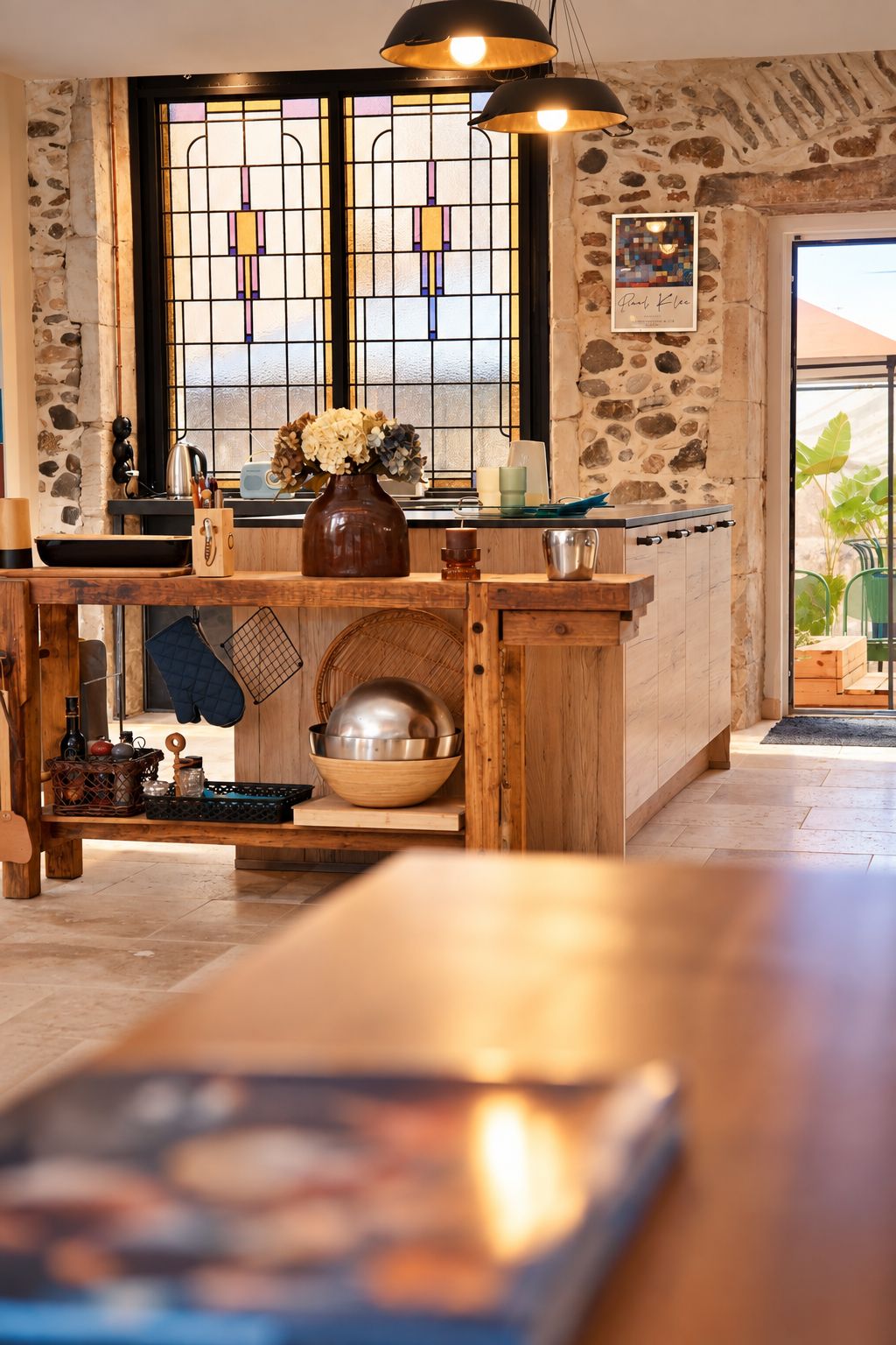 A kitchen with a wooden island, stone walls, a window with a grid pattern, and a hanging light fixture.
