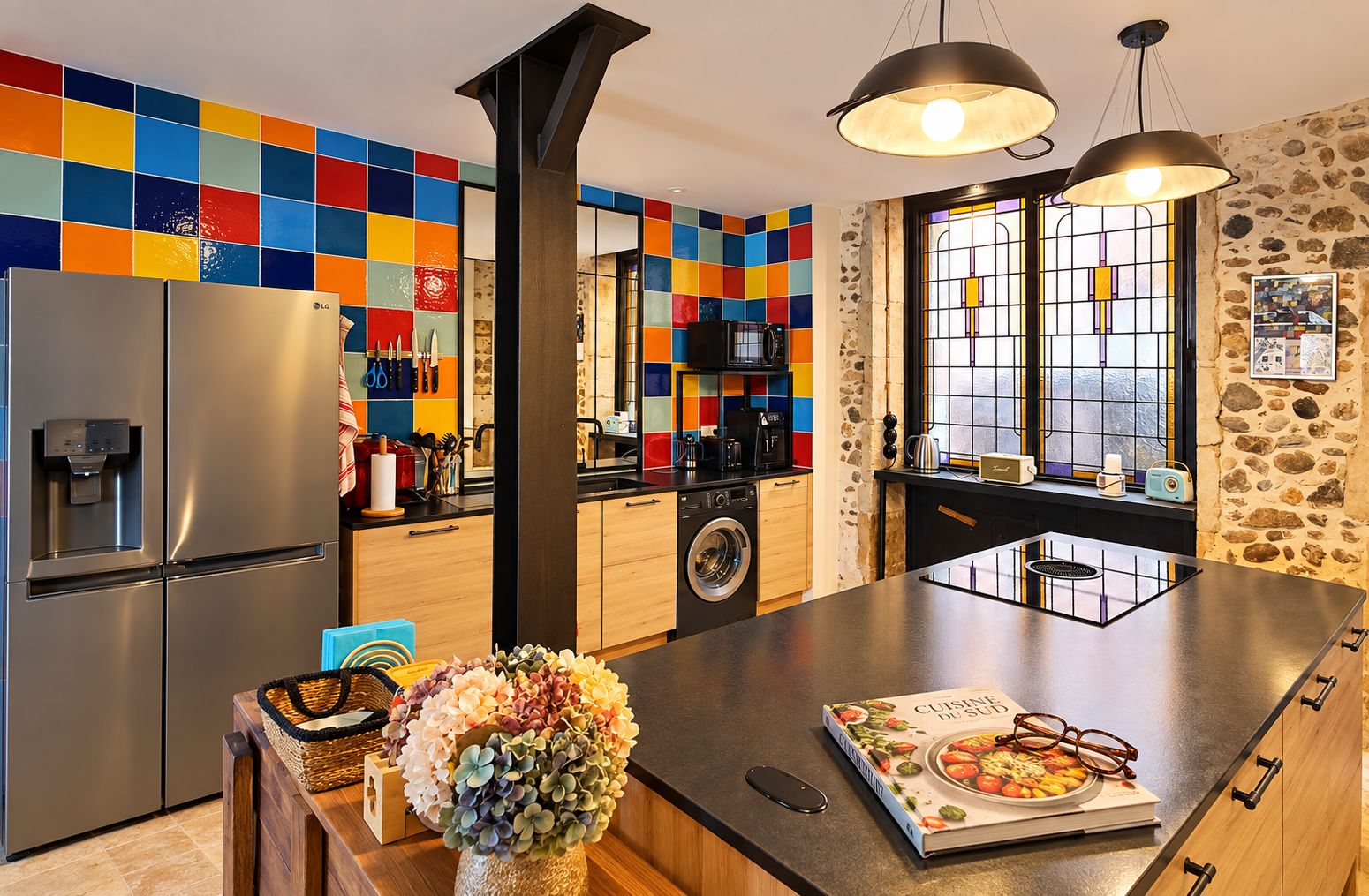 Una cucina moderna con frigorifero in acciaio inox, lavatrice integrata e un'isola spaziosa con un libro e dei bicchieri sopra.