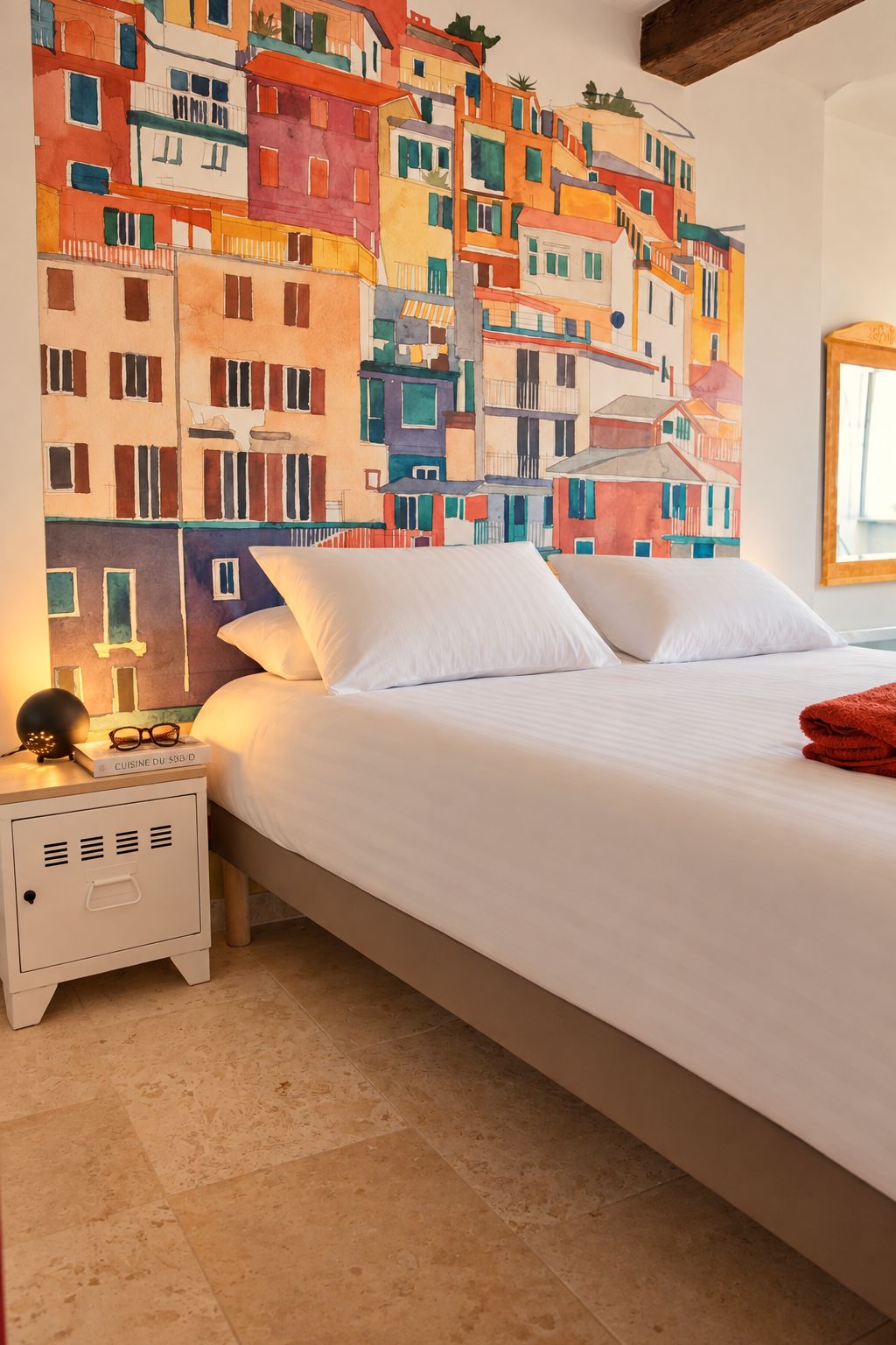 Une chambre d’hôtel avec un lit, une table de chevet, une lampe et une fresque murale aux couleurs vives.