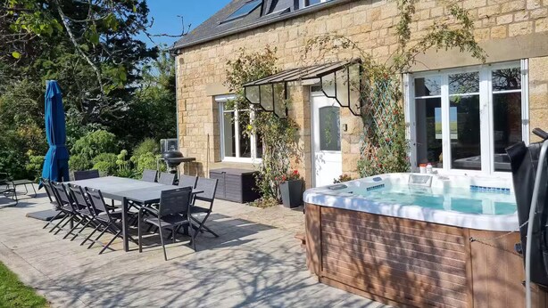 Une maison en pierre dotée d’un patio, d’un espace salon extérieur et d’un jacuzzi.