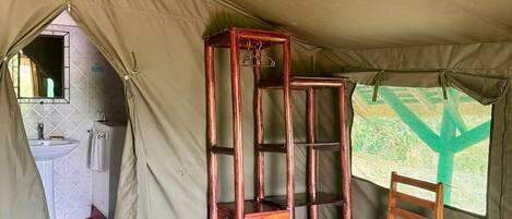 A tented room with a bed, a wooden chair, a small table, and a window with a view.