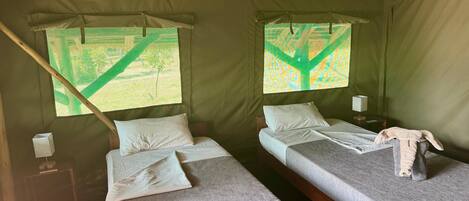 A tent with two beds, each with pillows and a blanket. There is a small table with a lamp and a box on it.