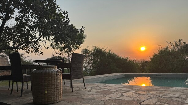 A stone pool with a wicker chair and table, surrounded by trees and a sunset view. - Bwana Tembo Safari Camp (Pakwach)