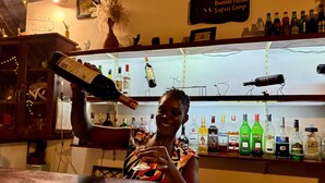 A bar area with a variety of liquor bottles on shelves and a person holding a bottle. - Bwana Tembo Safari Camp (Pakwach)
