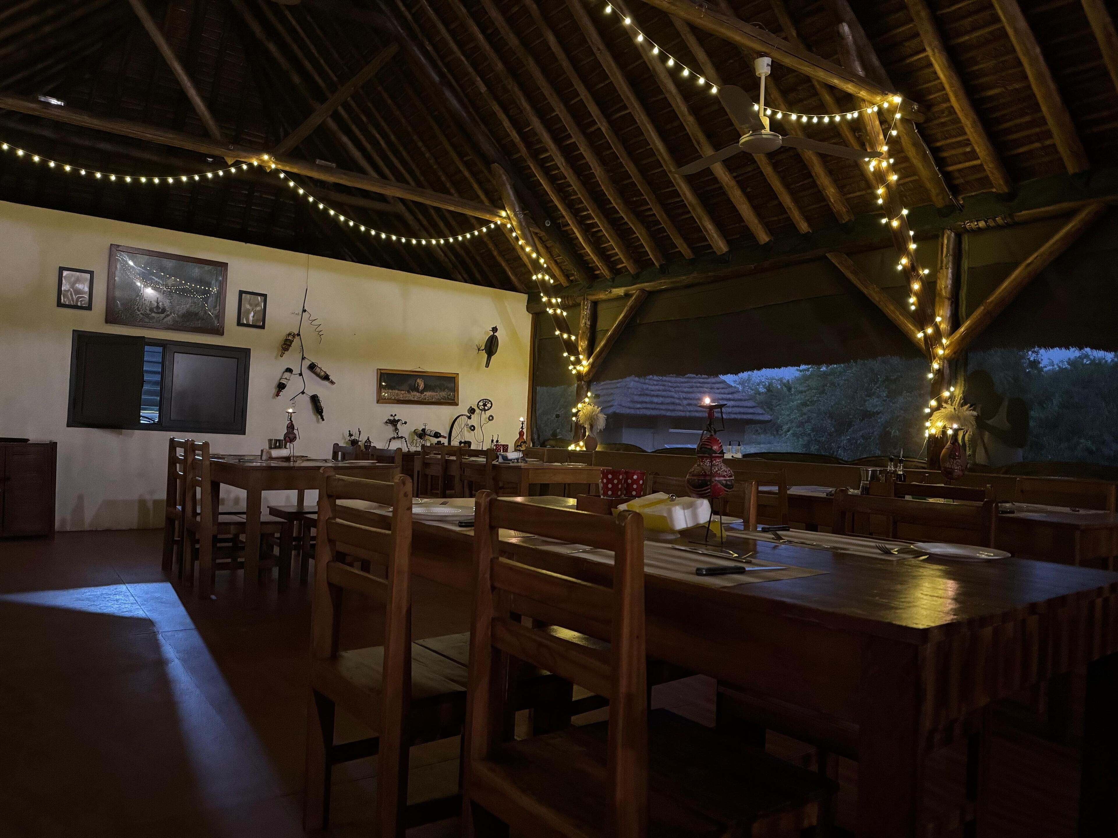 A dining area with wooden tables and chairs, string lights, and wall art.