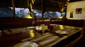 A dining area with tables set for two, featuring a decorative centerpiece and a view of trees outside. - Bwana Tembo Safari Camp (Pakwach)