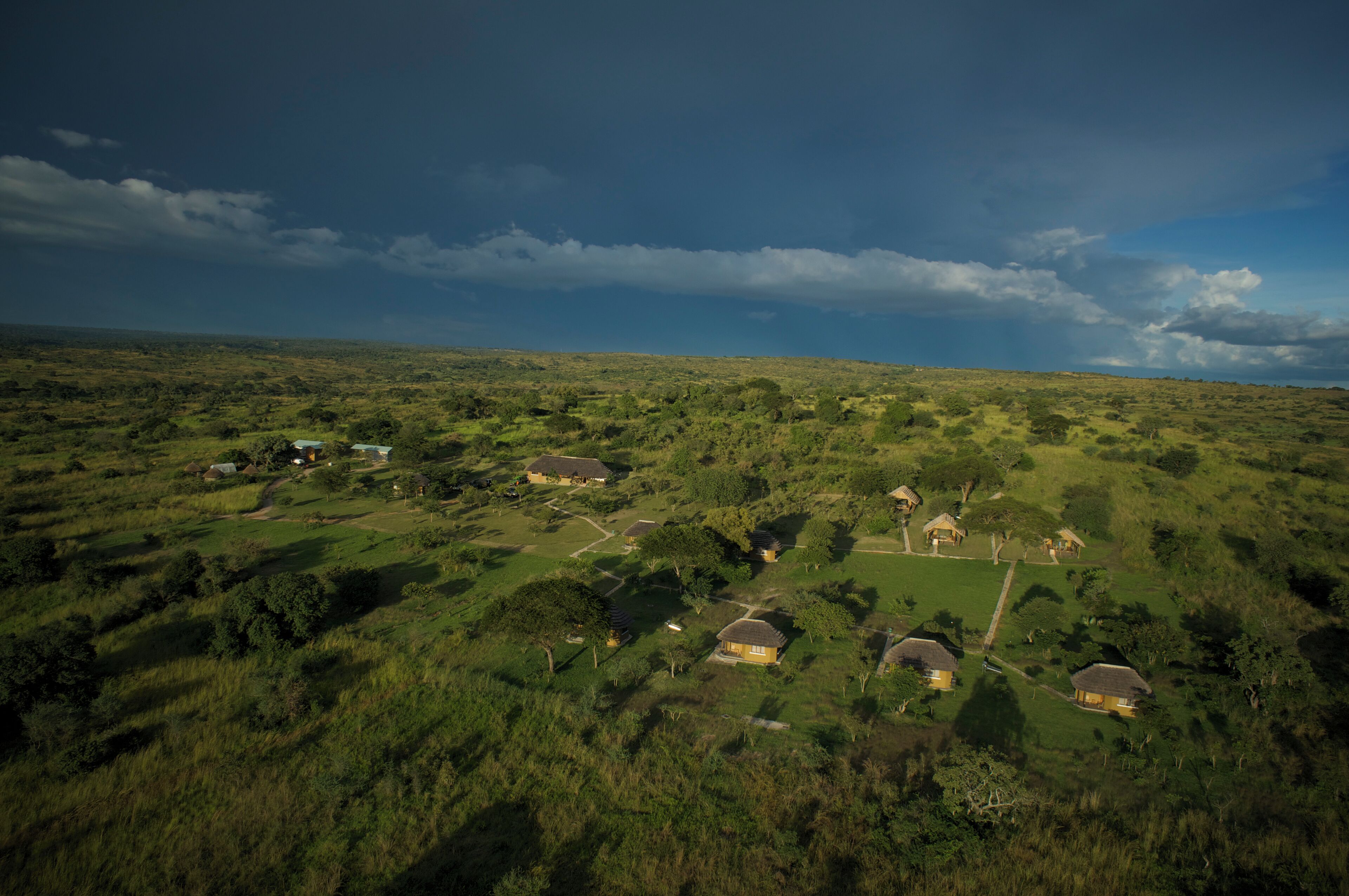 Paisagem rural com casas dispersas, rodeada por vegetação e um céu nublado.