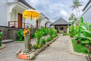 Una estatua de una figura sosteniendo un paraguas en un patio con senderos de piedra y plantas tropicales.