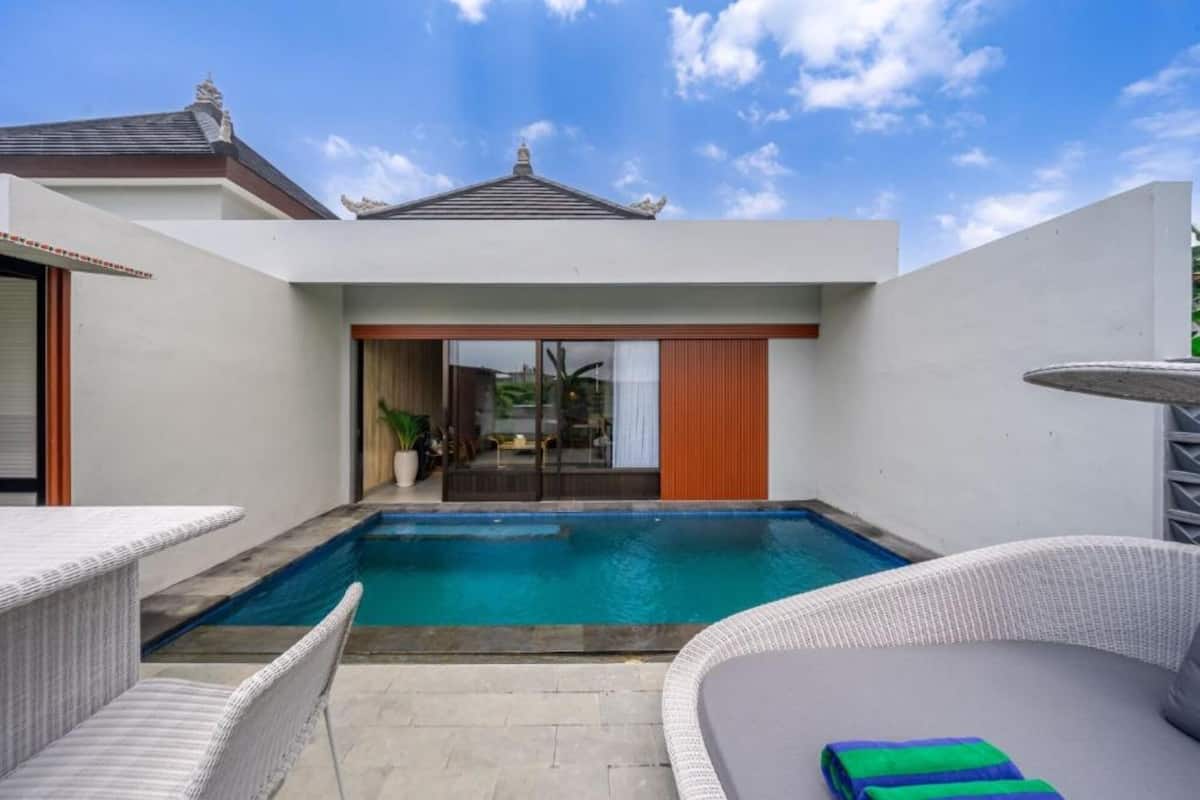 A modern outdoor pool area with a clear view of the sky, a covered patio, and a glimpse of the surrounding architecture.