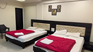 Camera d'albergo con due letti, ognuno con copripiumino rosso e bianco, e una testiera in legno scuro. Si vede una sedia e un lampadario fissato al muro.
