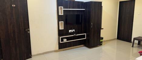 A hotel room with a large wardrobe, a flat-screen TV, a clock, and a bed with a red blanket.