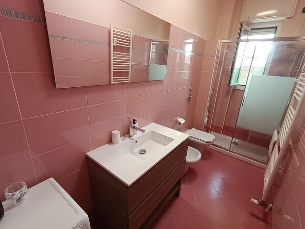 A modern bathroom with pink tiles, a white sink, a mirror, and a glass shower enclosure. - Giulia's sweet home near Rho Fiera (Pero)
