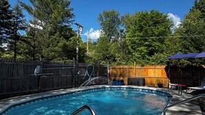 A swimming pool with a metal ladder, surrounded by a wooden fence and trees. - Cortland Riverfront Retreat (Cortland)