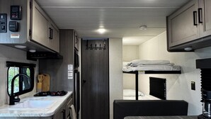 A compact RV kitchen with a sink, stove, and overhead cabinets. - Cortland Riverfront Retreat (Cortland)
