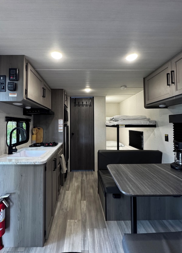 A compact RV kitchen with a sink, stove, and overhead cabinets. - Cortland Riverfront Retreat (Cortland)
