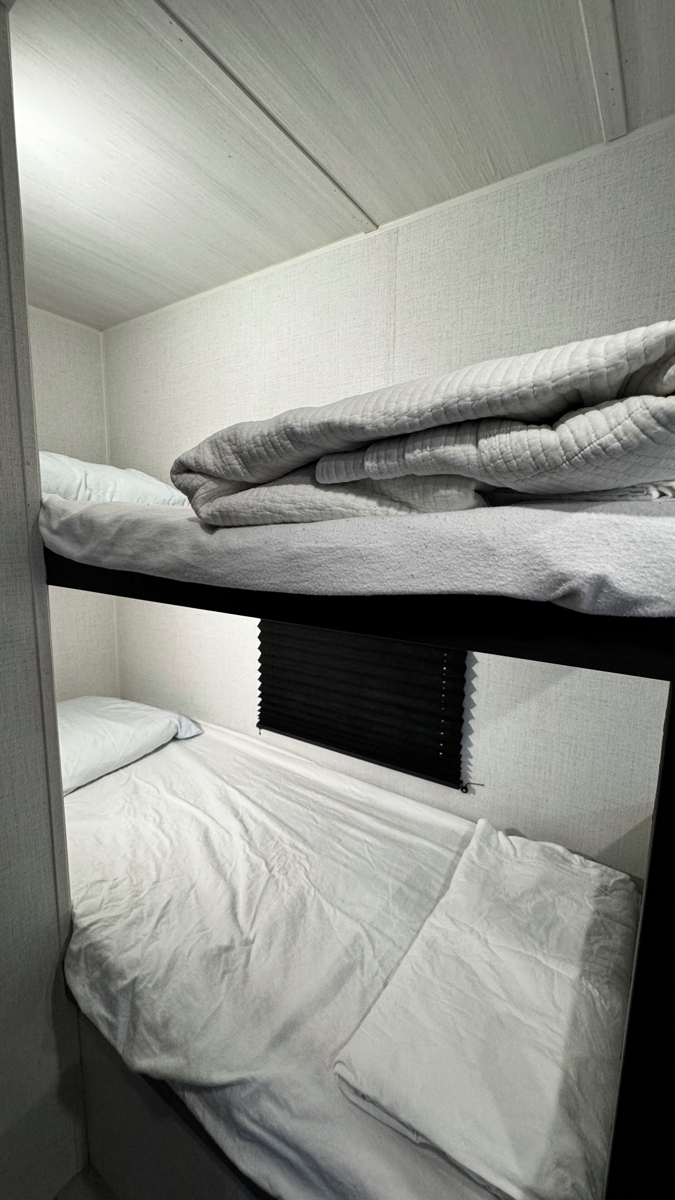 Een stapelbed met witte beddengoed en een zwart hoofdeinde.
