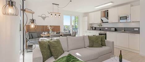 A modern living room with a sofa, a coffee table, and a kitchen area with white cabinets and a microwave.