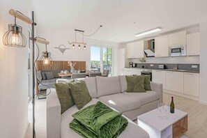 A modern living room with a sofa, a coffee table, and a kitchen area with white cabinets and a microwave.